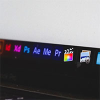 A photograph of a MacBook Pro laptop with the Adobe Creative Cloud Suite and Final Cut Pro in the menu on the screen