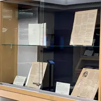A photograph of display cases for the Poetry at Miami exhibition. Several books and pages are propped up in the display cases with small label cards adjacent to them. There are large panels in each of the cases behind the items with headers for the different themes and eras for the pieces in that case. The one closest to the camera reads: The Black experience, 1960-1980