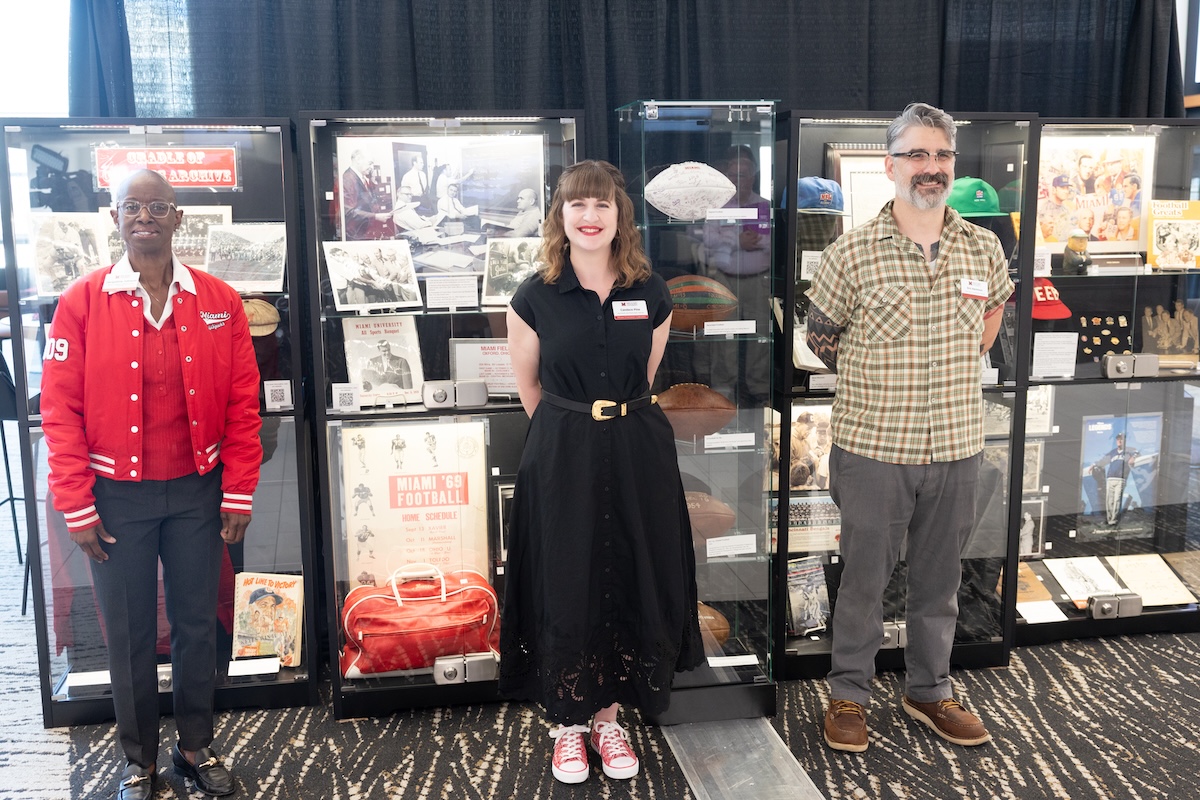 Jacky Johnson, Candace Pine, and Eric Harrelson standing in front of display cases full of Cradle of Coaches artifacts from the Miami University collections